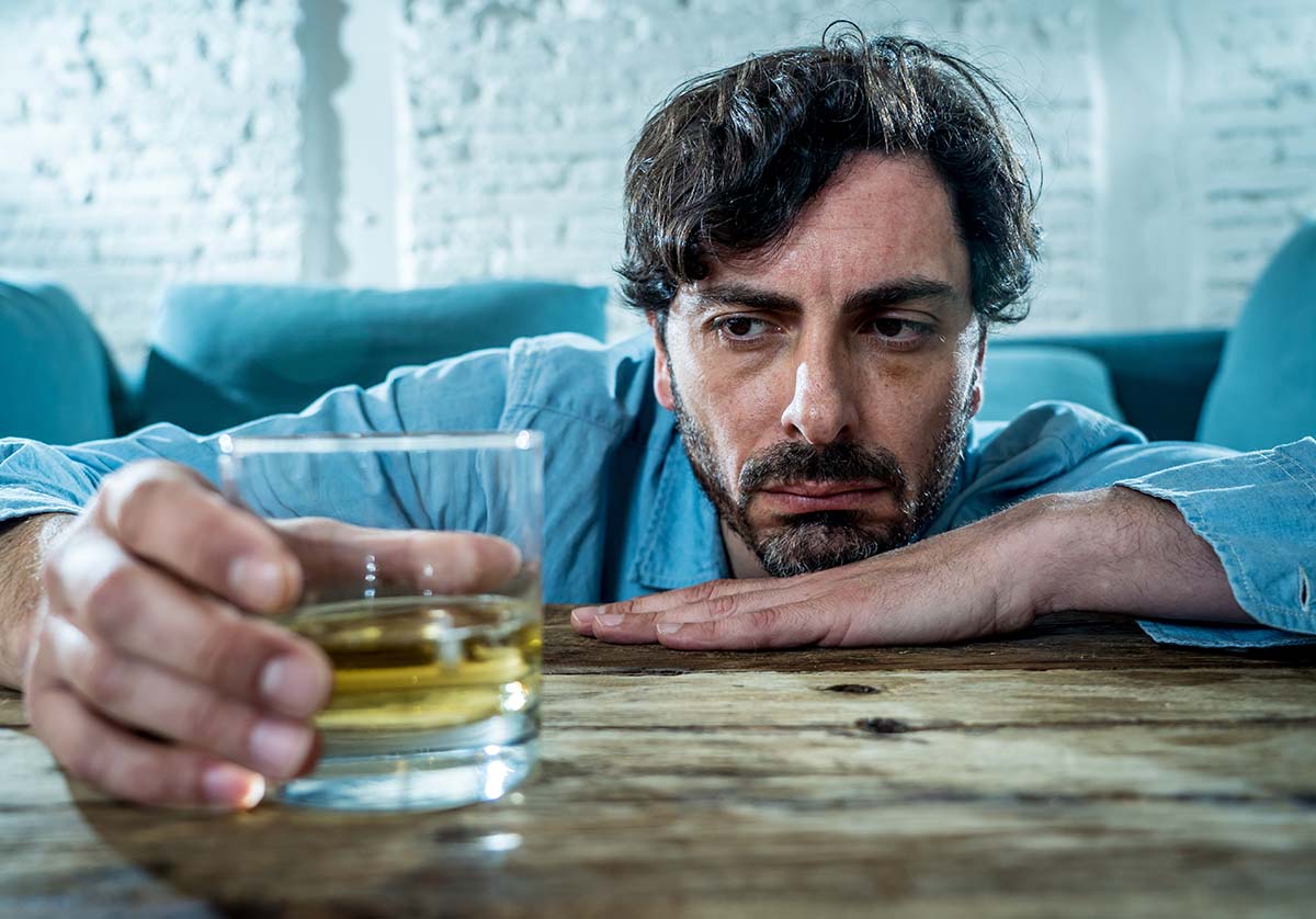 a man with an addiction to alcohol and depression holds a glass of amber colored liquid
