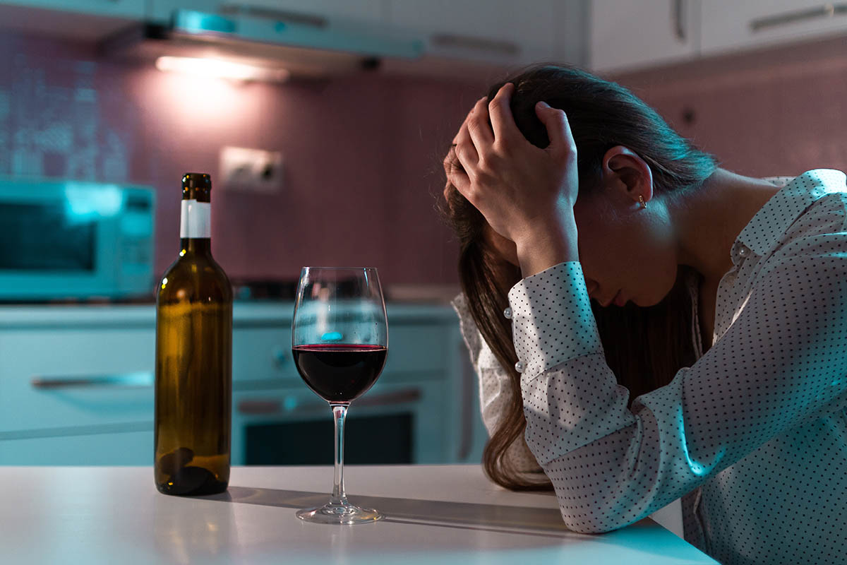 a woman sits next to a bottle of wine holding her head and wondering am i an alcoholic