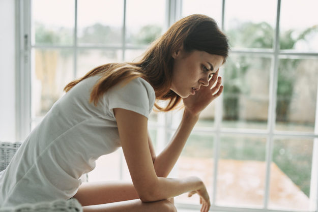 a woman sits next to a window and wonders do i need addiction treatment