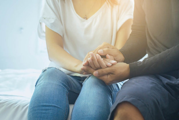 two people hold hands as they wonder how to help a loved one with addiction