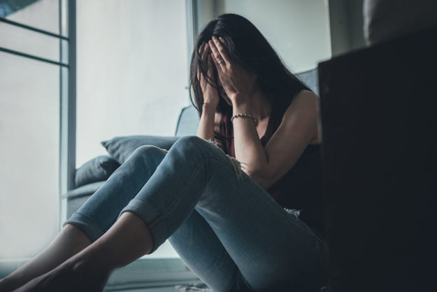 a woman covers her face as she wonders about the difference between a panic attack vs. an anxiety attack