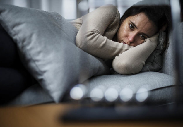 a woman lies on a couch and wonders how to help a loved one with depression